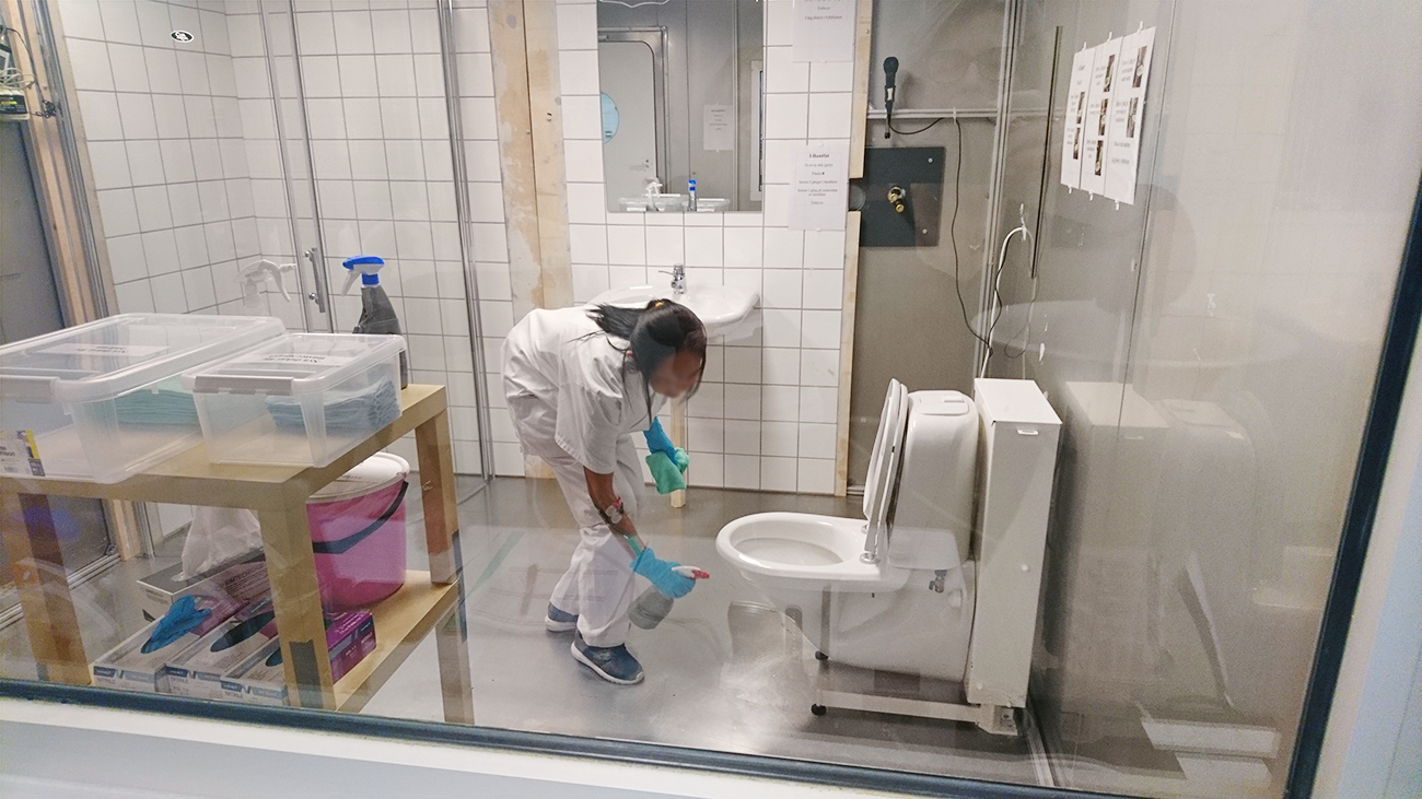 person städar en toalett i en laboratoriemiljö. Foto.