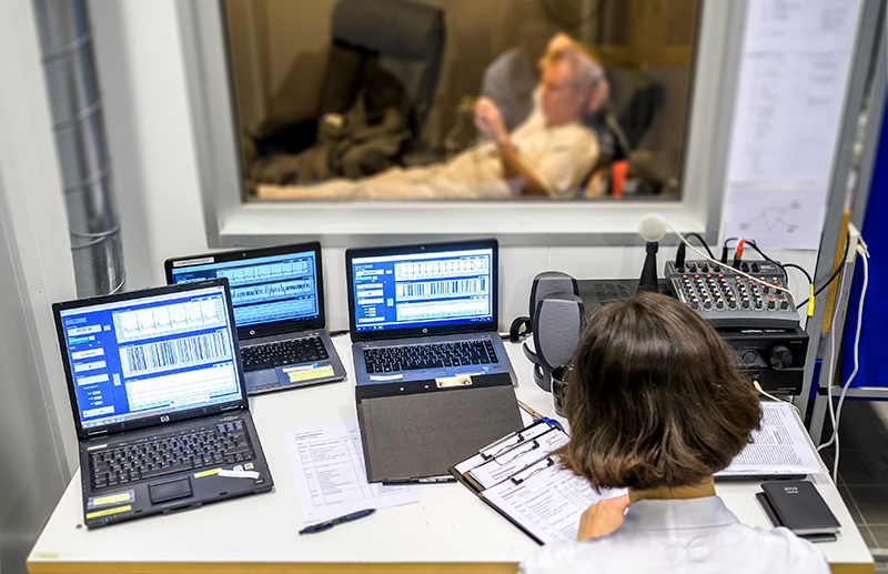 en person sitter i aerosolkammaren, i förgrunden syns datorer med mätdata och en person i vit rock