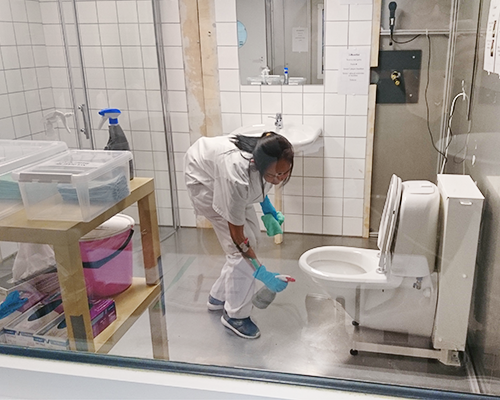 person städar ett badrum i en labbmiljö. Foto. 